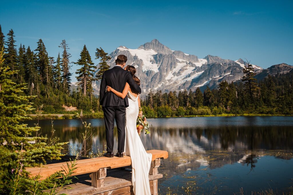 Bride and groom stand on a dock by an alpine lake during their North Cascades elopement photos