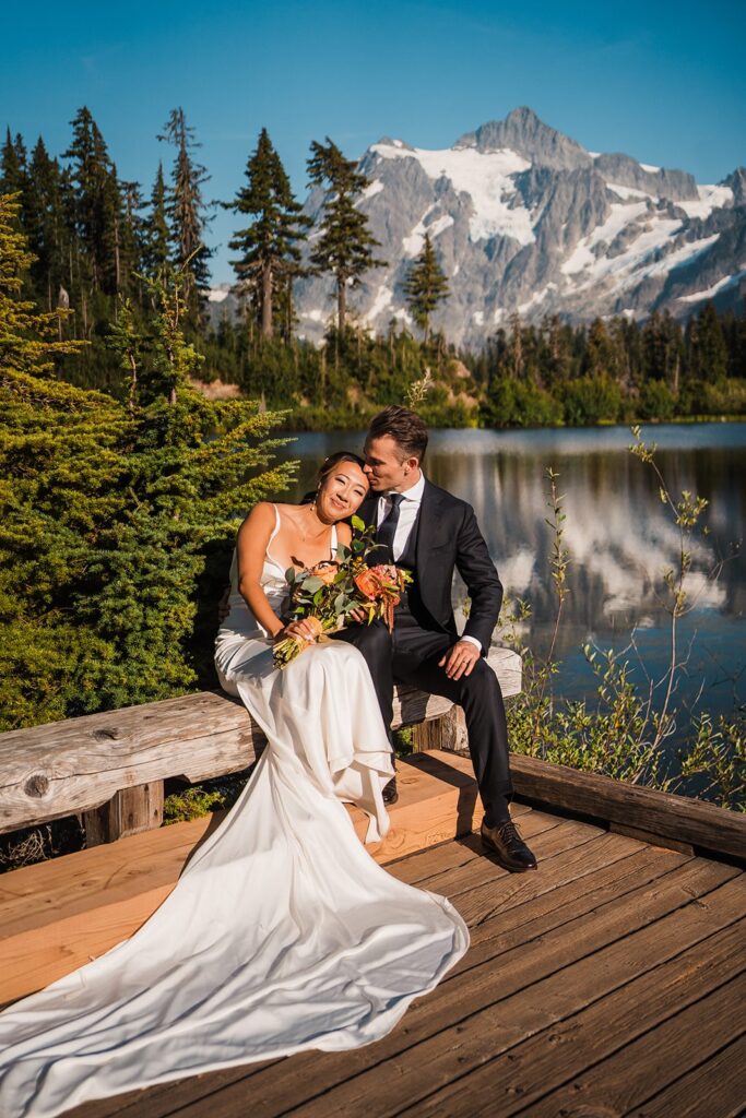 Bride and groom sit on a dock during their North Cascades elopement by an alpine lake