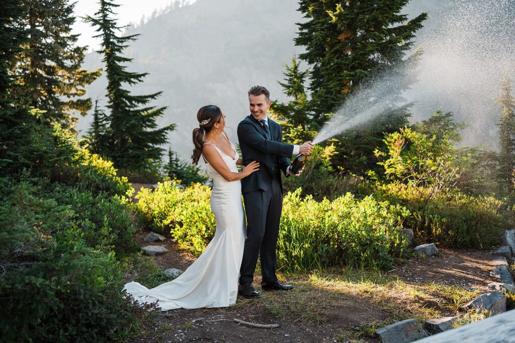 Bride and groom spray champagne during their elopement picnic in the North Cascades