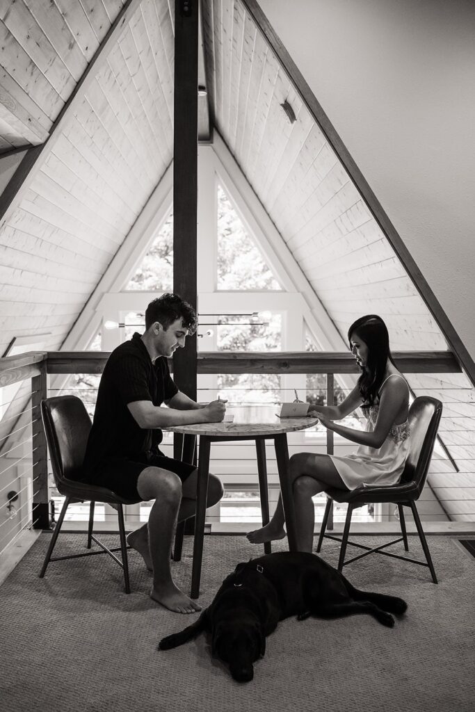 Bride and groom sit at a table in their A-Frame cabin writing their wedding vows