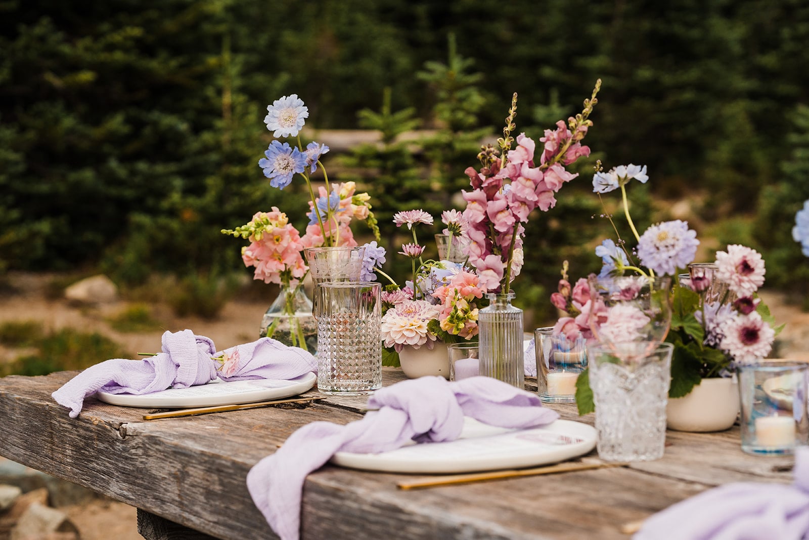 Pastel flowers in bud vases sit on top of a wood picnic table at a day use area at one of the top Washington state park wedding venues.