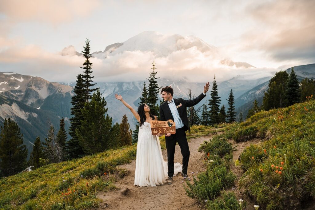 Bride and groom cheer while holding their custom Mount Rainier wedding sign 