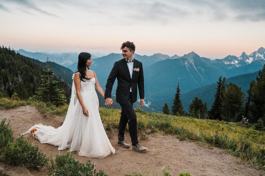 Bride and groom hold hands while walking around the mountain trail during their sunset photos at Mount Rainier