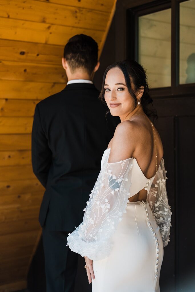 Bride looks back over her should before her wedding first look with groom at their Airbnb cabin