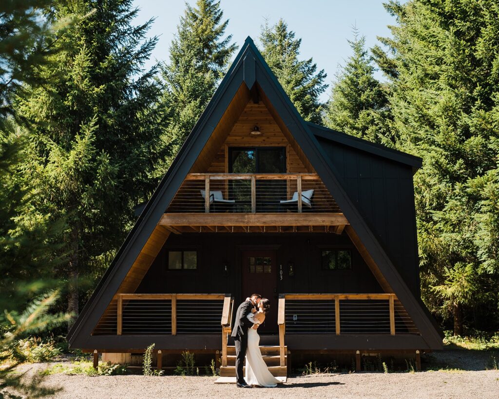 Bride and groom kiss in front of an A-frame cabin during their alpine lake elopement in Washington