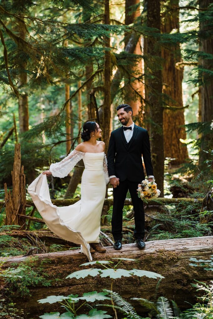 Bride and groom stand on a fallen log during their elopement photos in the forest in Washington