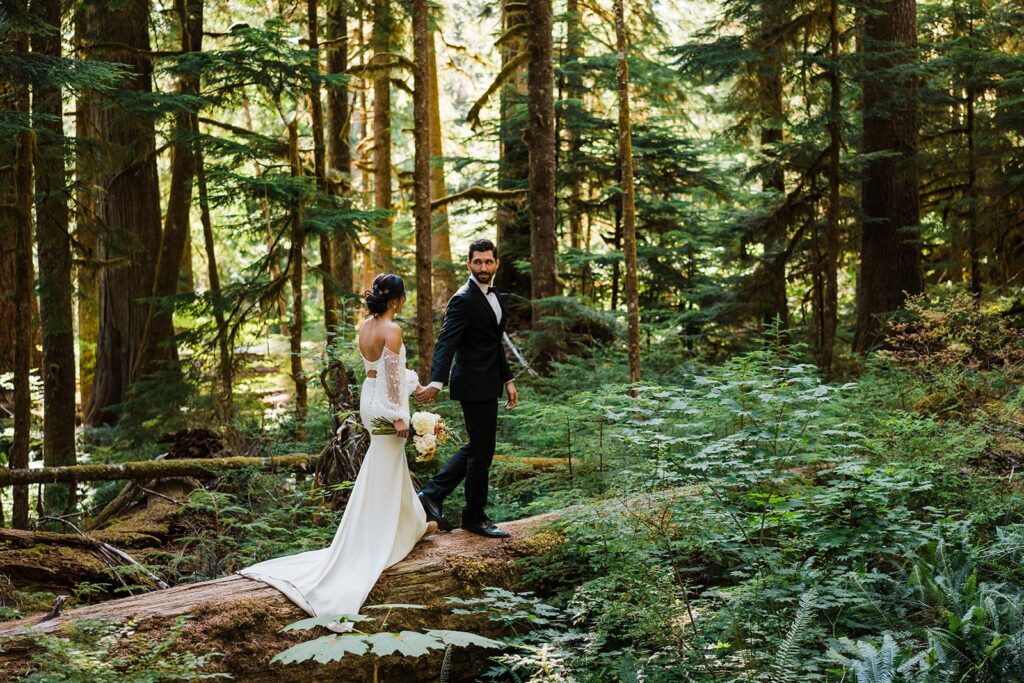 Bride and groom walk across a fallen log in the forest during their elopement photos in Washington