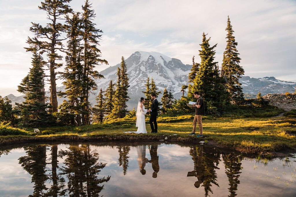 Bride and groom hold hands while exchanging vows at their alpine lake elopement ceremony