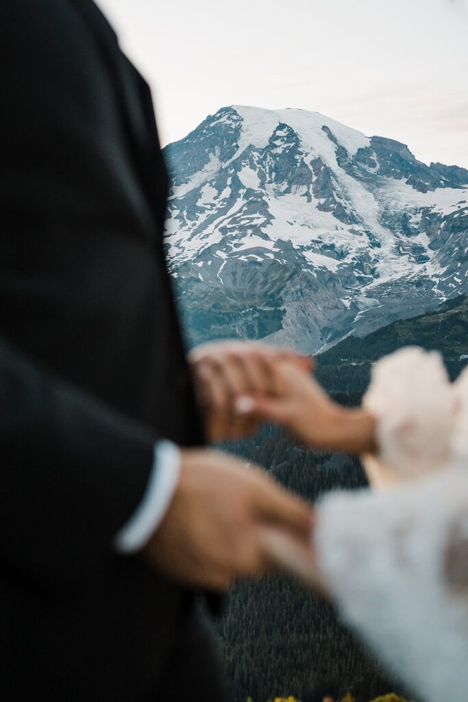Bride and groom hold hands in front of Mt Rainier during their alpine lake elopement