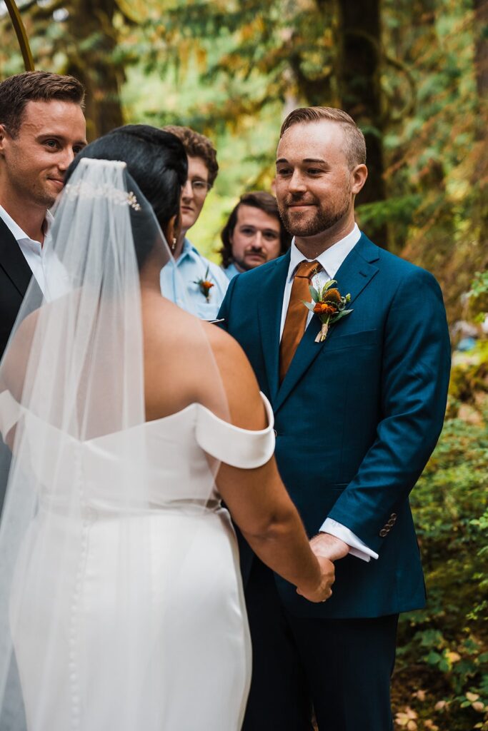 Groom smiles at bride during their forest elopement ceremony in the North Cascades