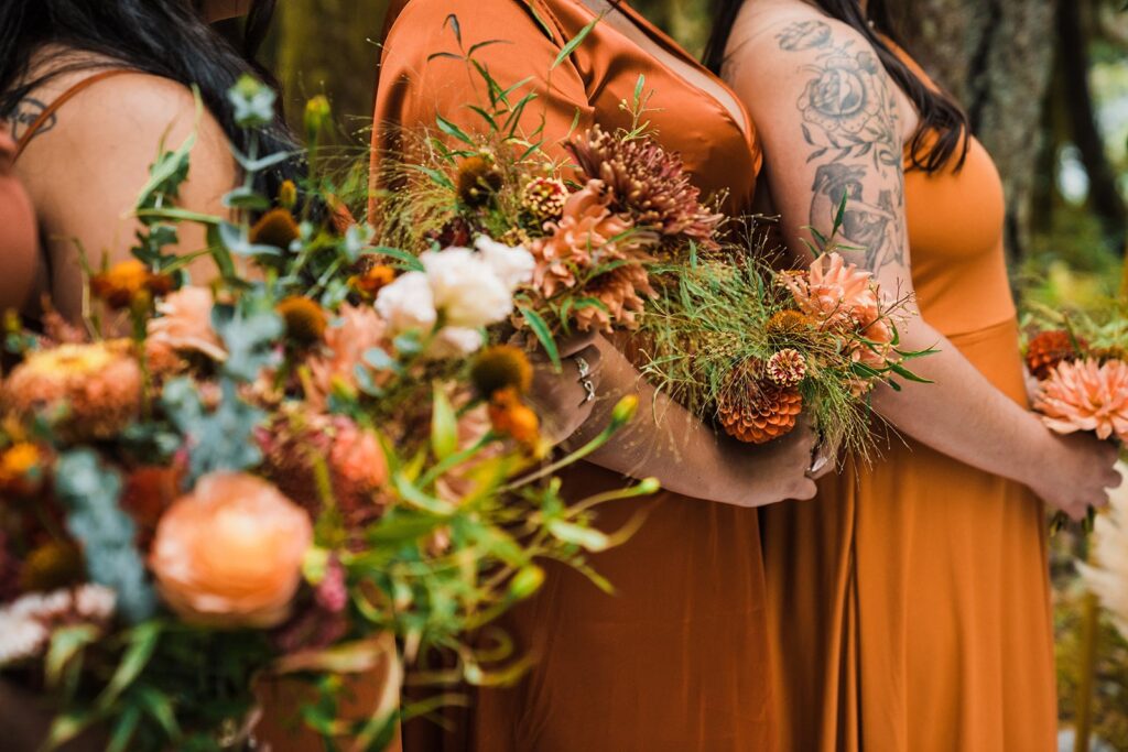 Bridesmaids wearing orange bridesmaid dresses and holding autumn toned wedding bouquets