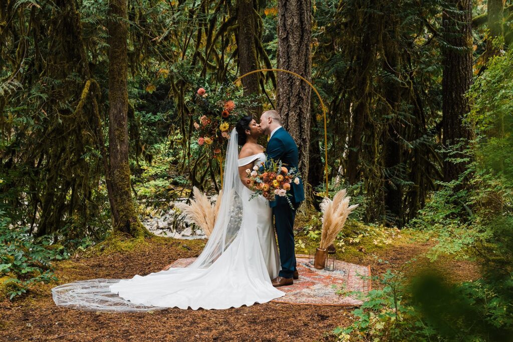 Bride and groom kiss at the wedding altar in the forest during their family elopement