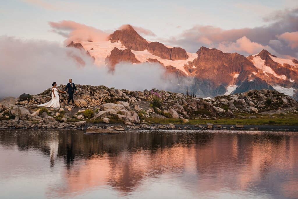Bride and groom hold hands while walking around an alpine lake during their North Cascades elopement
