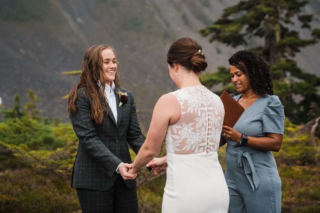 Brides hold hands during their rainy North Cascades wedding ceremony