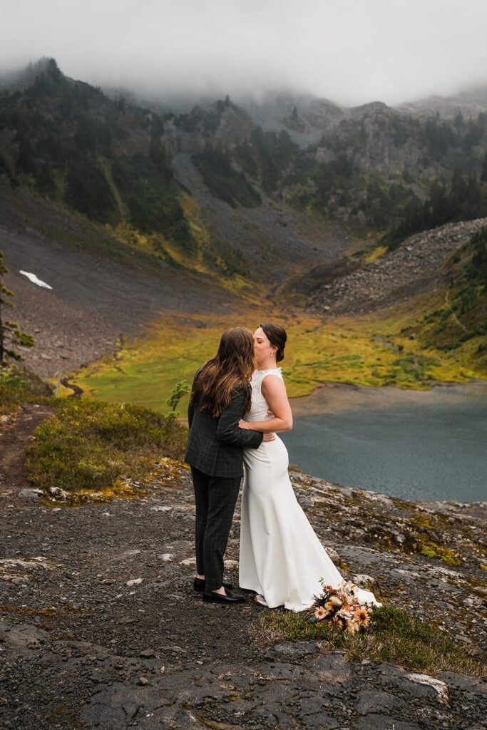 Brides kiss in front of an alpine lake in the North Cascades