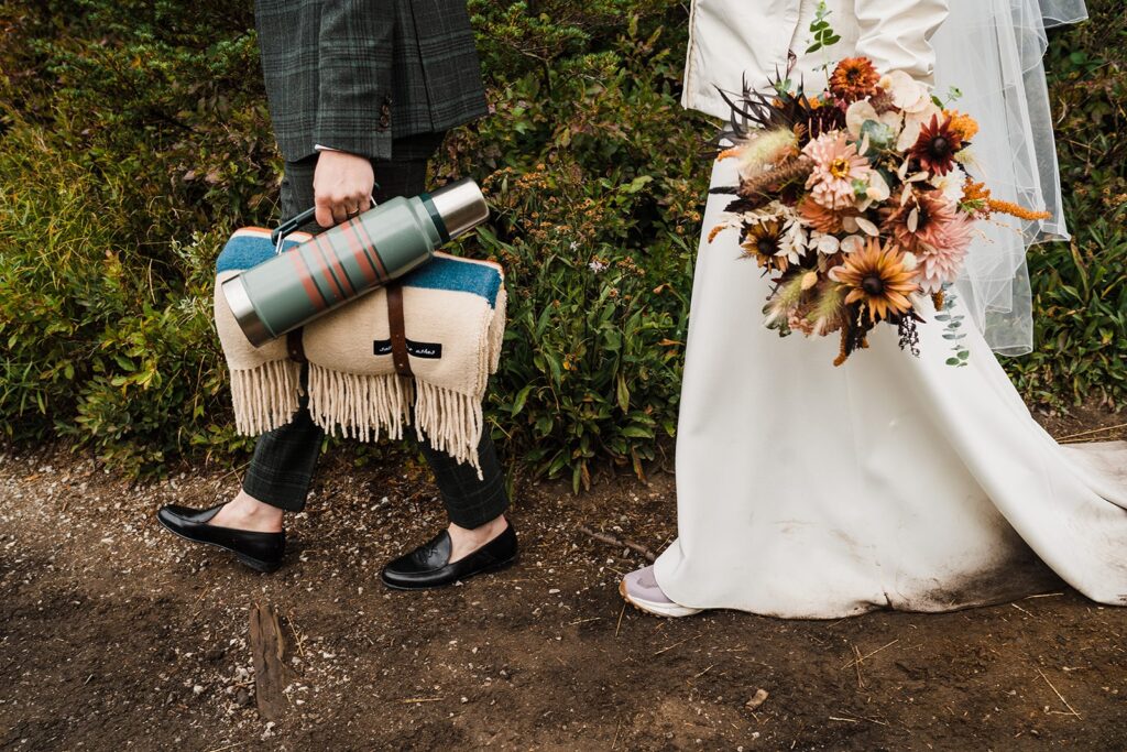 Brides hike with flowers and a blanket in the North Cascades