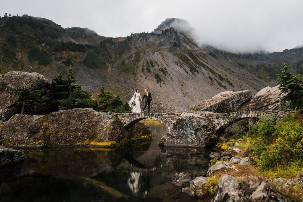 Brides hold hands while walking across a bridge in the North Cascades