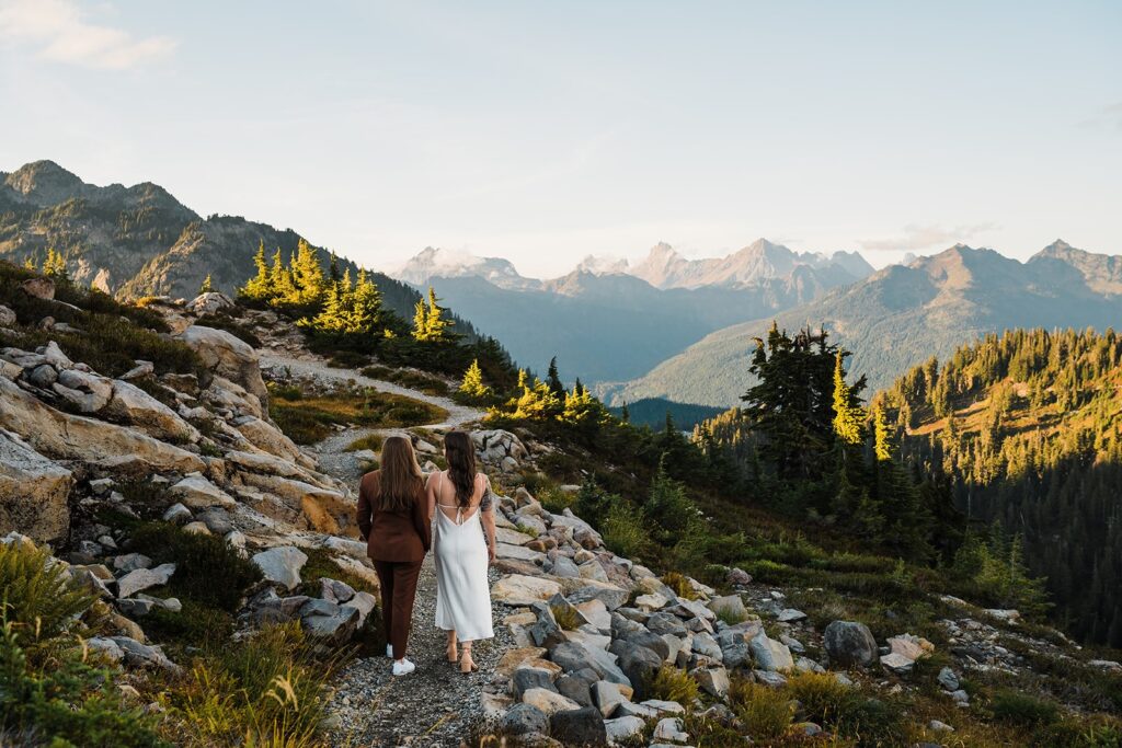 Brides hold hands while walking along a mountain trail in the North Cascades