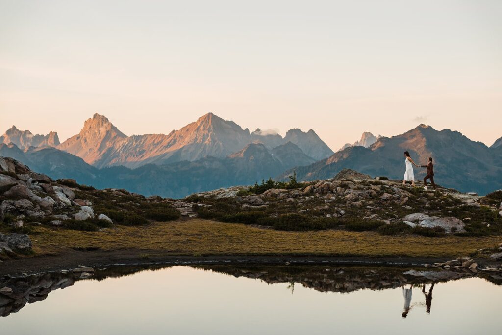 Brides hold hands while walking around an alpine lake in the North Cascades