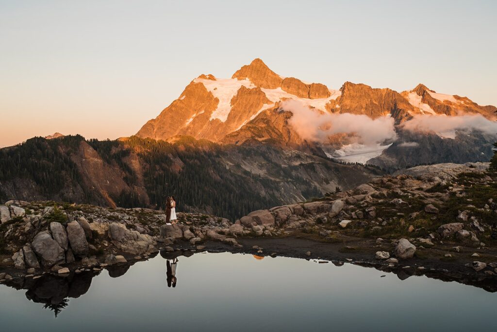 Brides kiss in front of an alpine lake in the North Cascades during sunset 