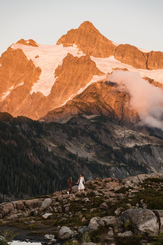Brides hold hands while walking across a mountain in the North Cascades