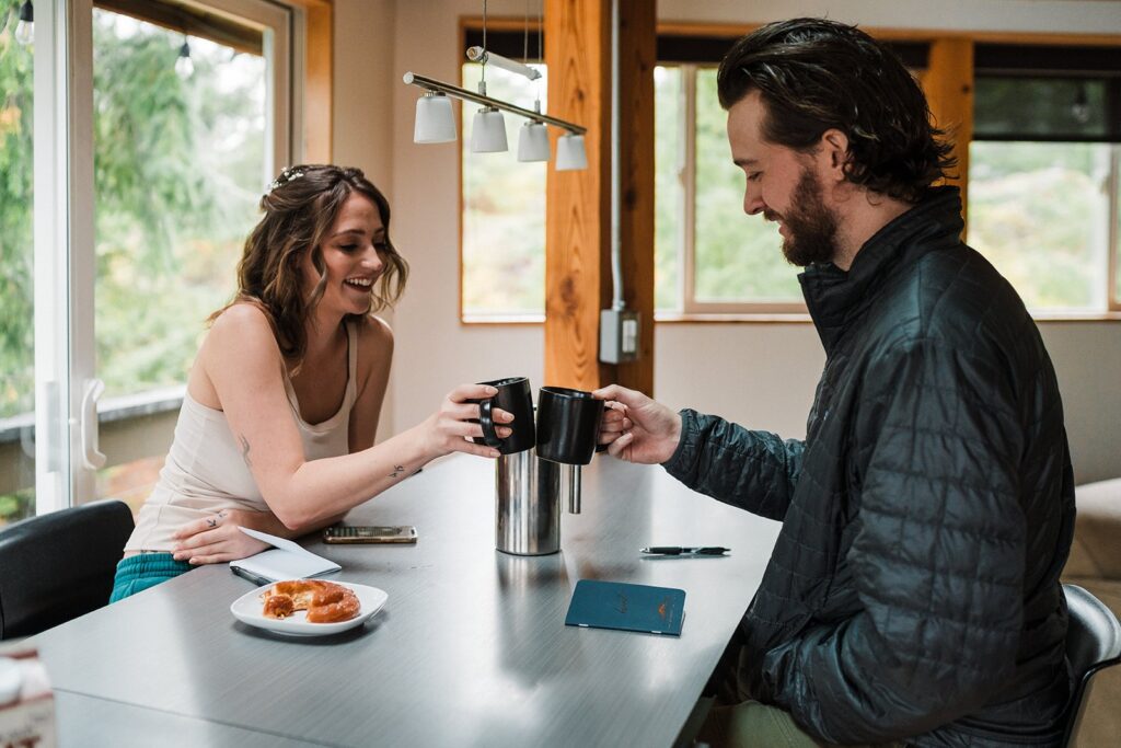 Bride and groom drink coffee at their cabin before getting ready for their forest elopement