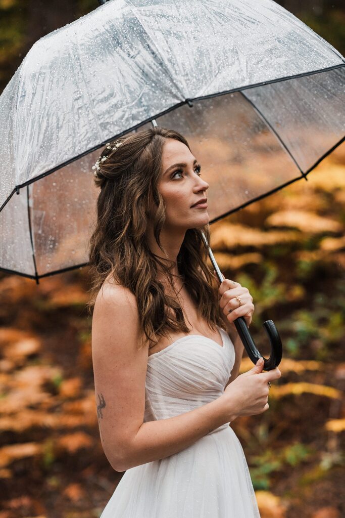 Bride holding clear umbrella during her rainy forest elopement in Snoqualmie