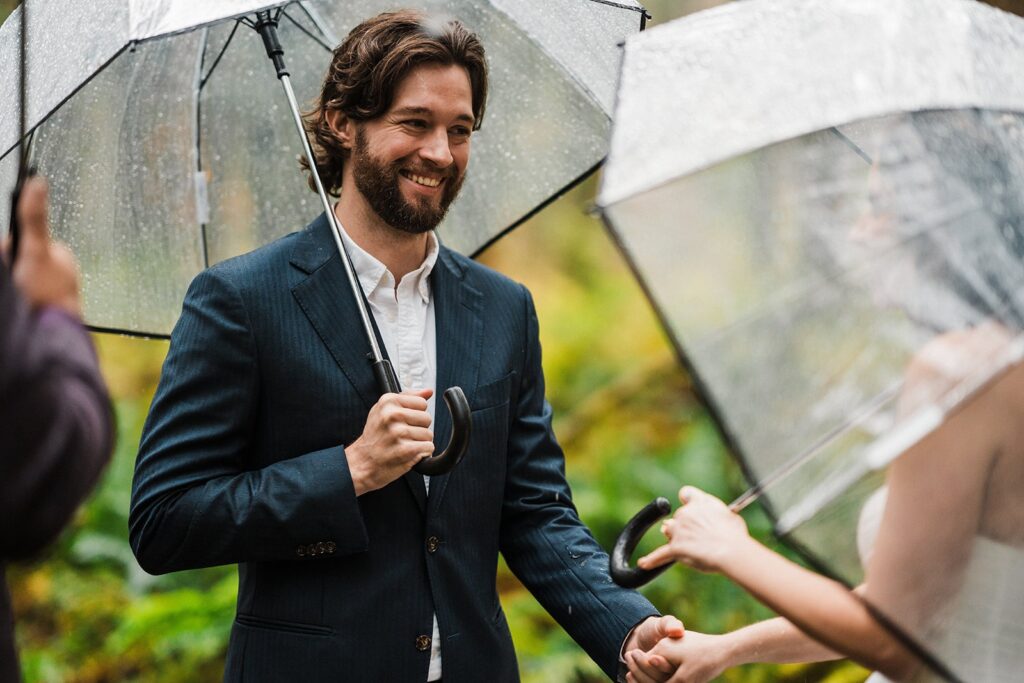 Groom smiles at bride while holding her hand during their rainy ceremony in Snoqualmie