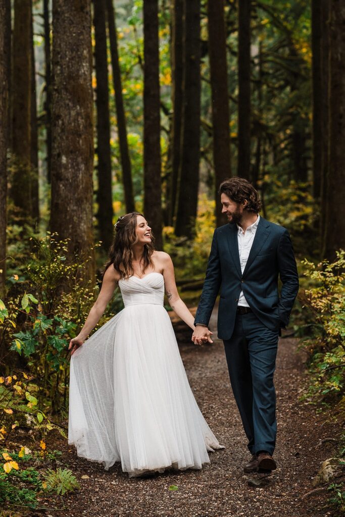 Bride and groom hold hands while walking through a forest trail for their elopement in Snoqualmie