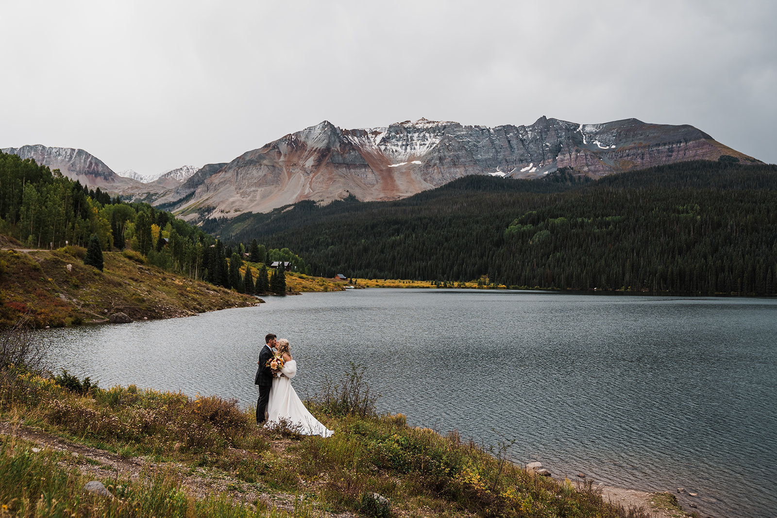 Bride and groom kiss in front of an alpine lake during their Telluride elopement
