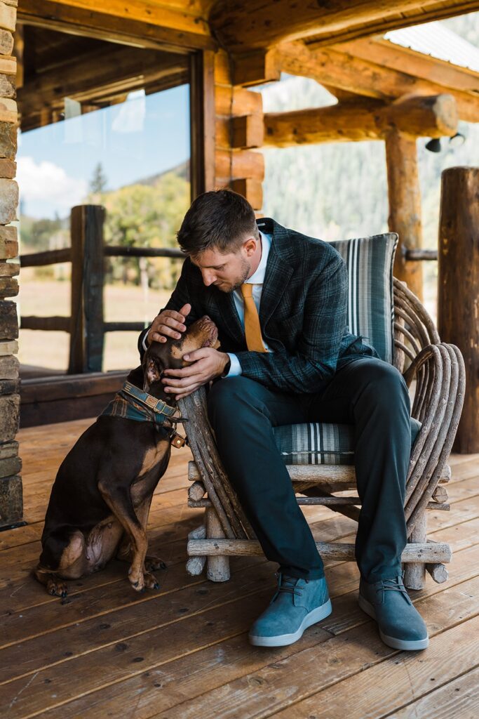 Groom pets dog while sitting in a rocker on the porch of his cabin in Telluride