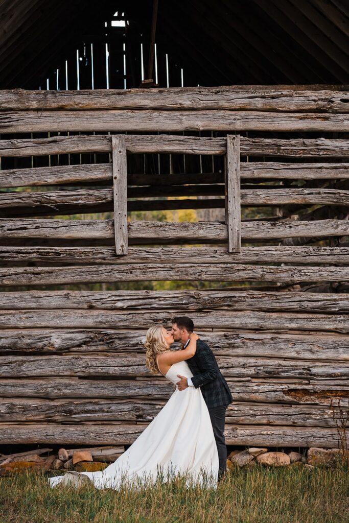 Bride and groom kiss in front of a wood barn in Telluride, Colorado