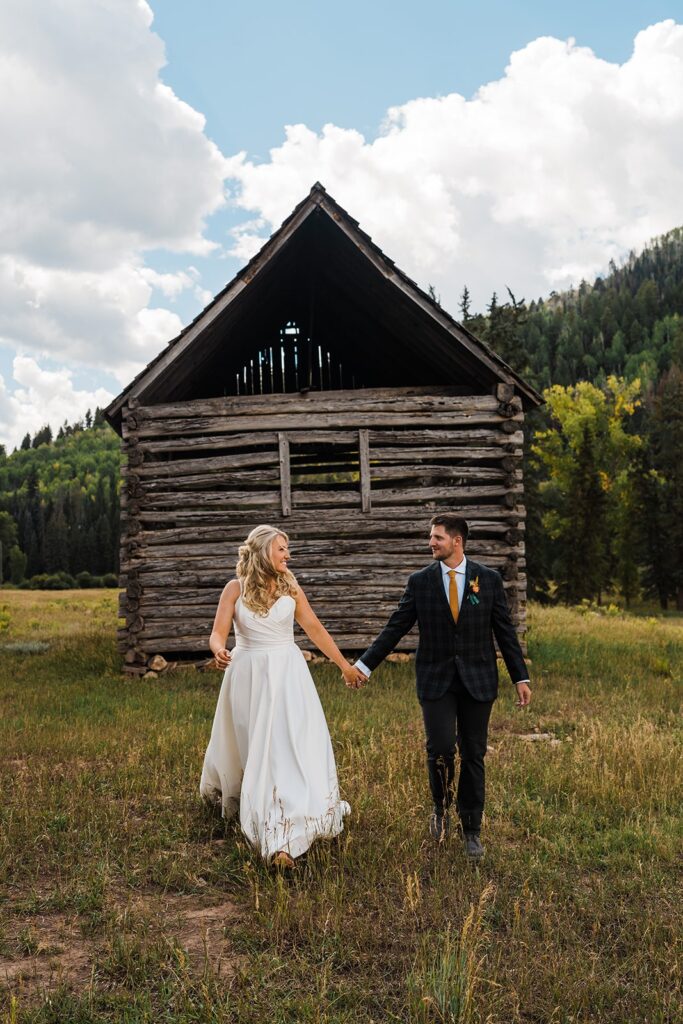 Bride and groom hold hands and walk through a field during after their Telluride elopement first look 