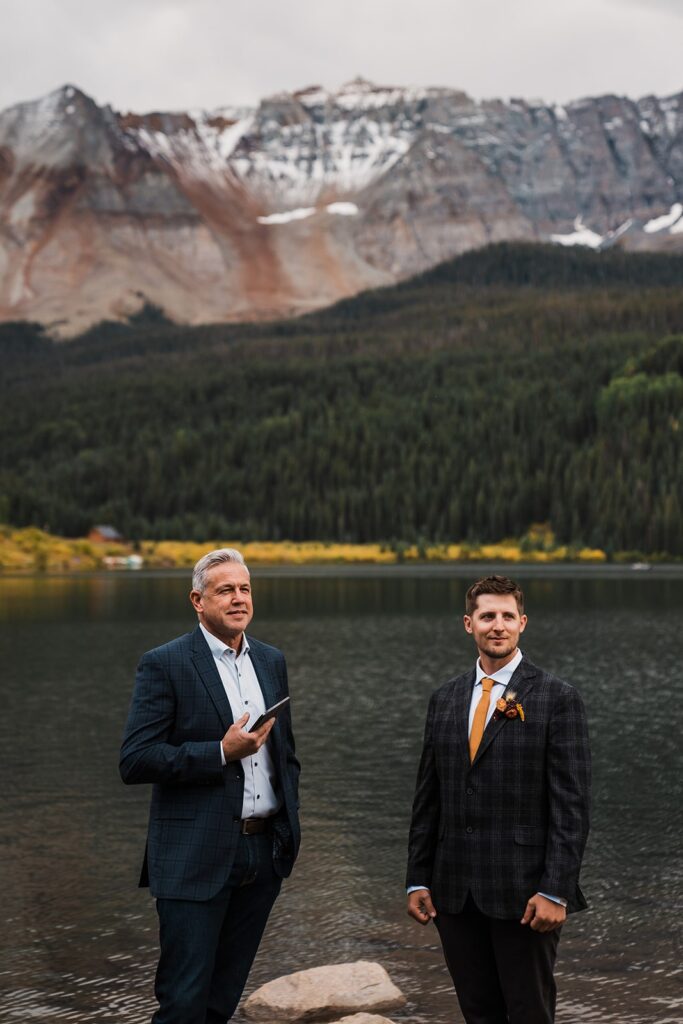 Groom stands by an alpine lake in Colorado waiting for the bride 