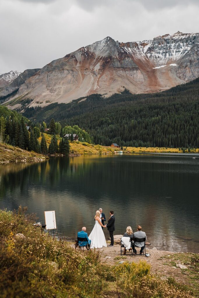 Bride and groom hold hands by an alpine lake during their Telluride elopement ceremony
