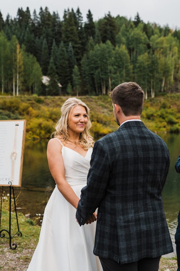 Bride and groom hold hands during their Telluride elopement ceremony by an alpine lake
