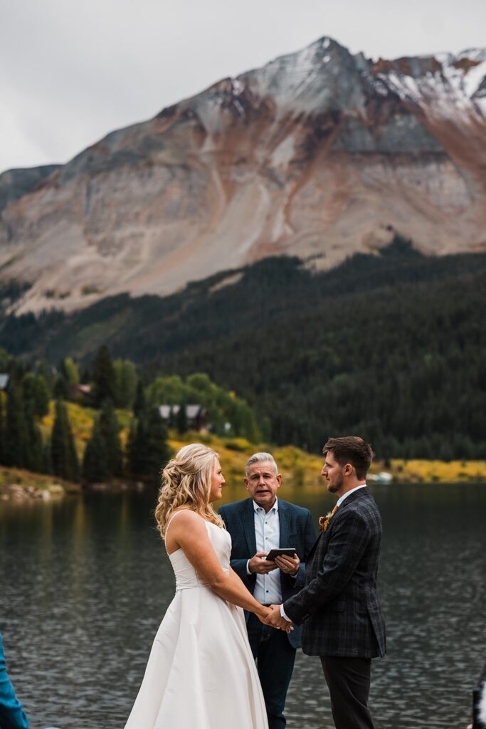 Bride and groom hold hands during their elopement ceremony by an alpine lake