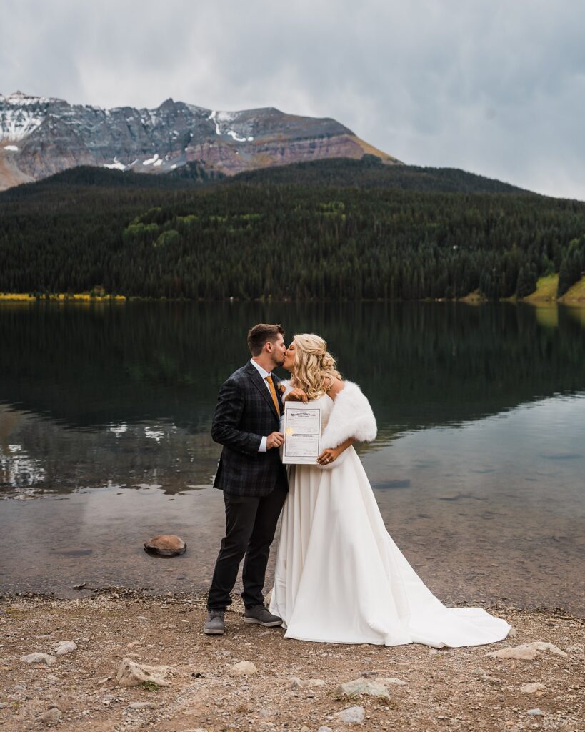 Bride and groom kiss by an alpine lake after signing their Colorado marriage license