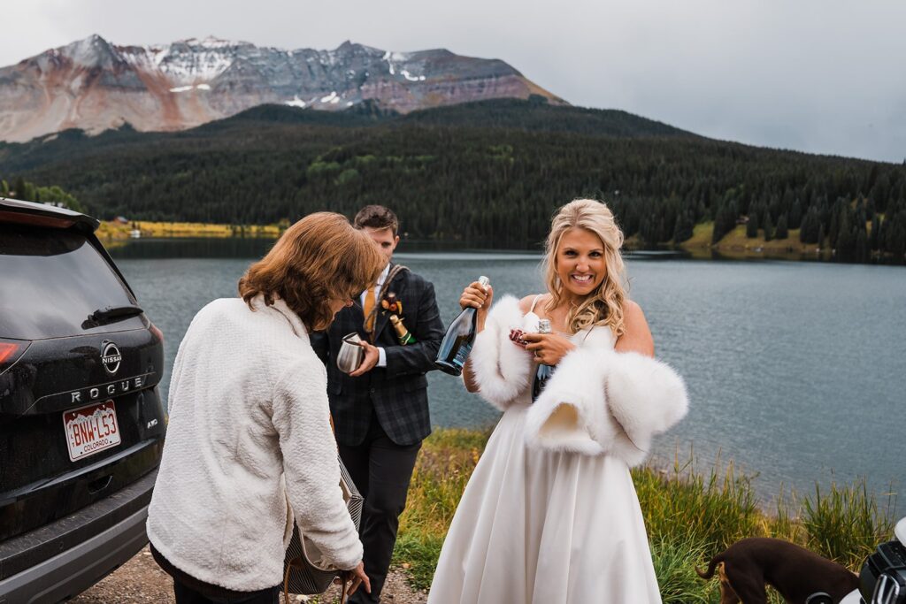 Bride smiles while holding a bottle of champagne after her Telluride elopement ceremony