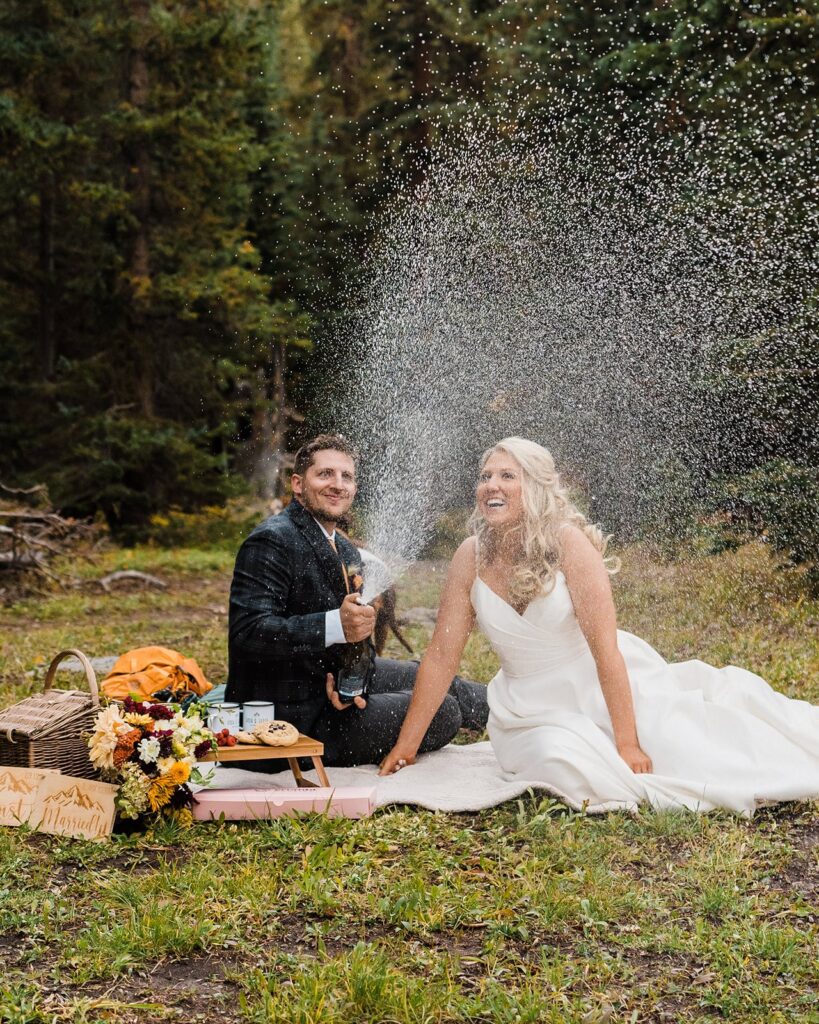 Bride and groom spray champagne during their mountain picnic in Telluride