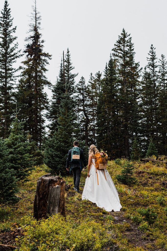 Bride and groom wearing hiking backpacks while walking through the trails in the Telluride mountains