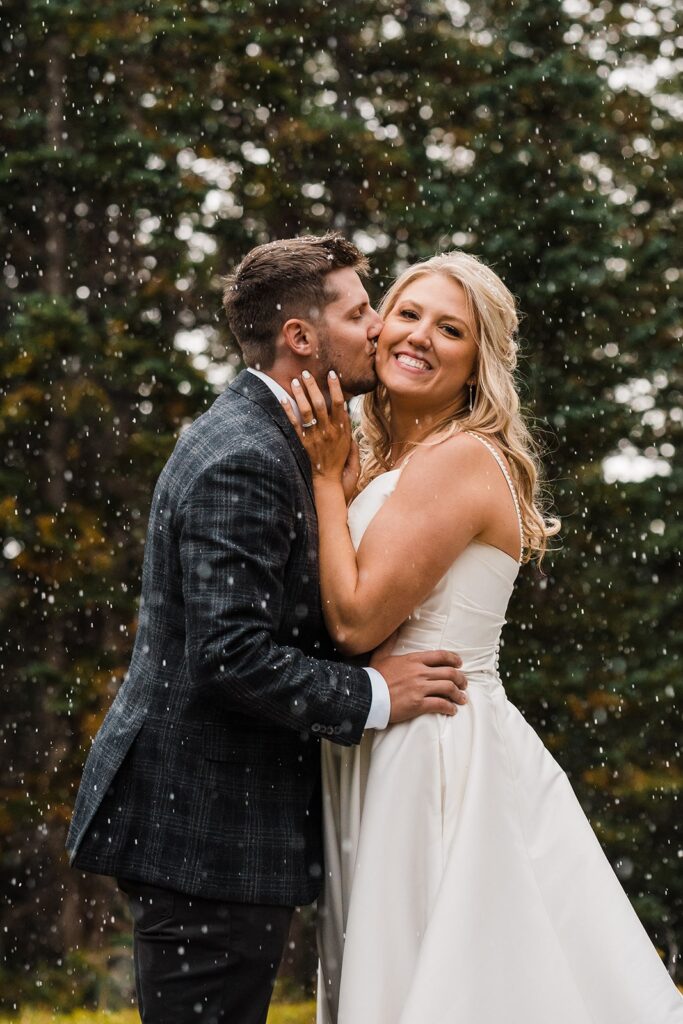 Groom kisses bride on the cheek while it snows during their elopement in Telluride