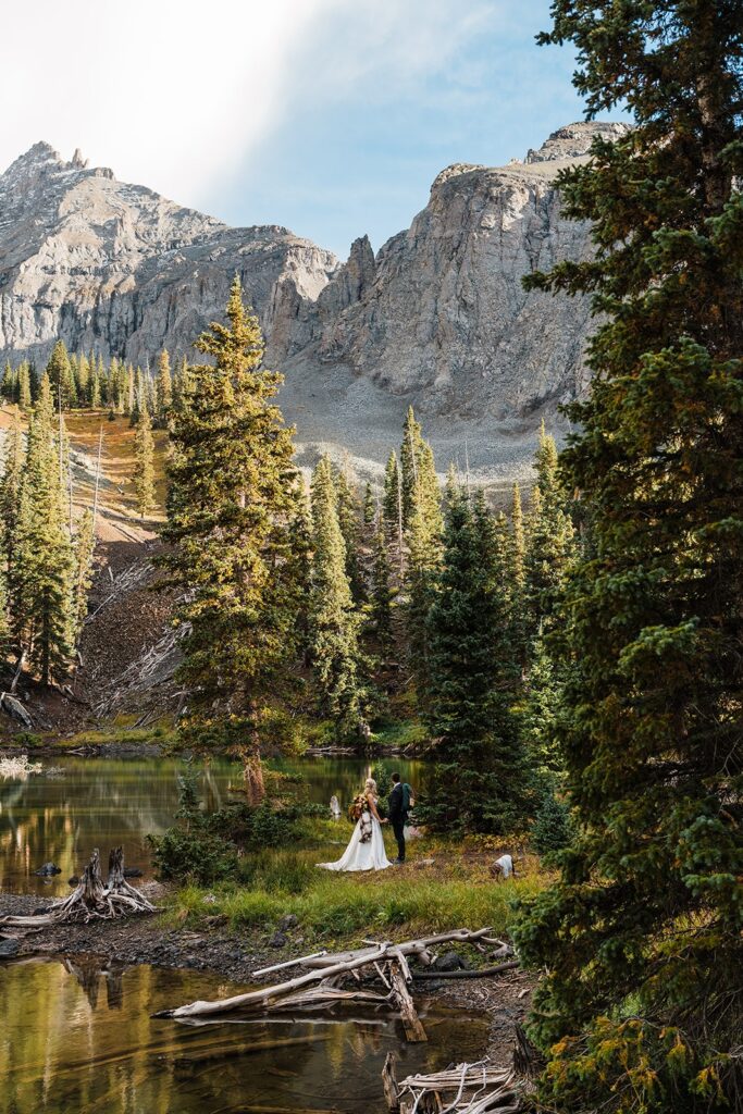 Bride and groom hold hands while standing by an alpine lake after their Telluride elopement