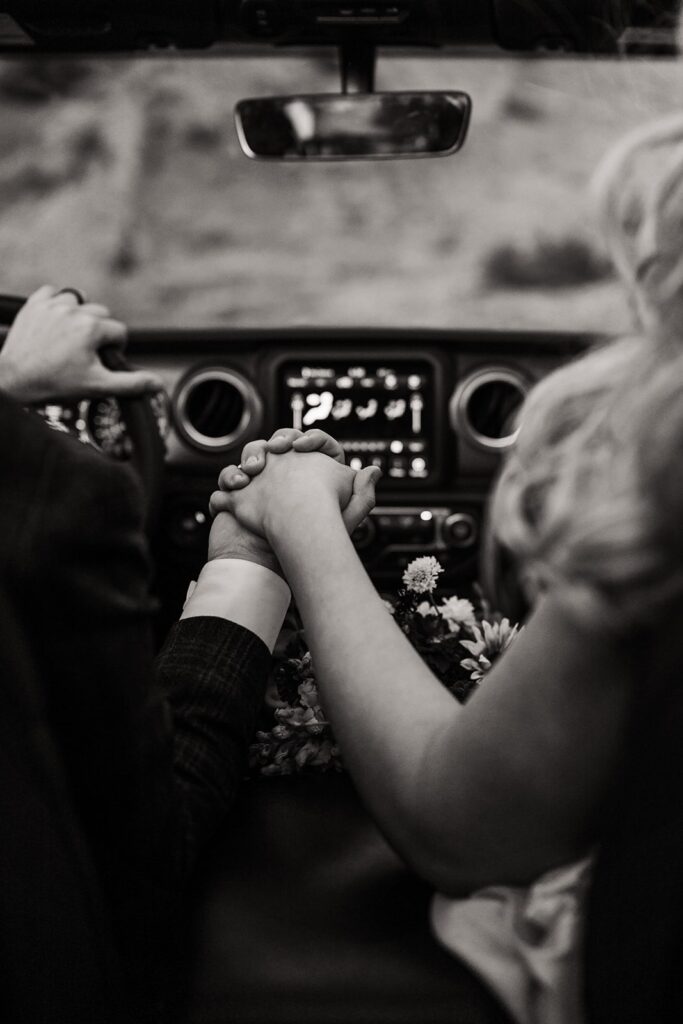 Bride and groom hold hands in their Jeep while going down the mountain