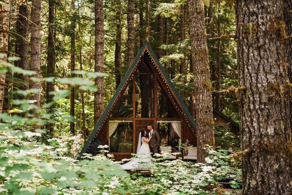 Bride and groom stand in front of their A-frame cabin in the woods in Washington