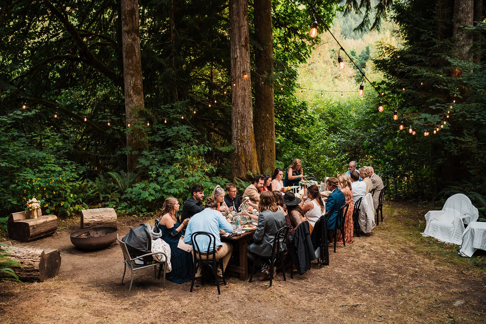 Friends and family gather around a Washington elopement reception in the forest under string lights