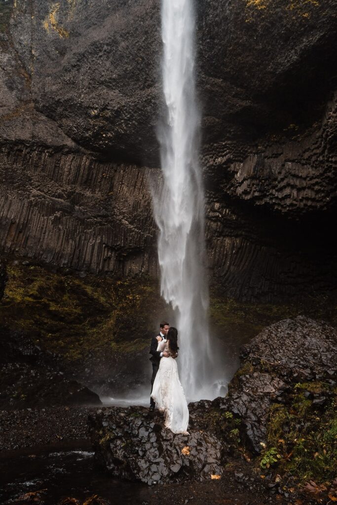 Bride and groom kiss in front of a waterfall during their Oregon elopement