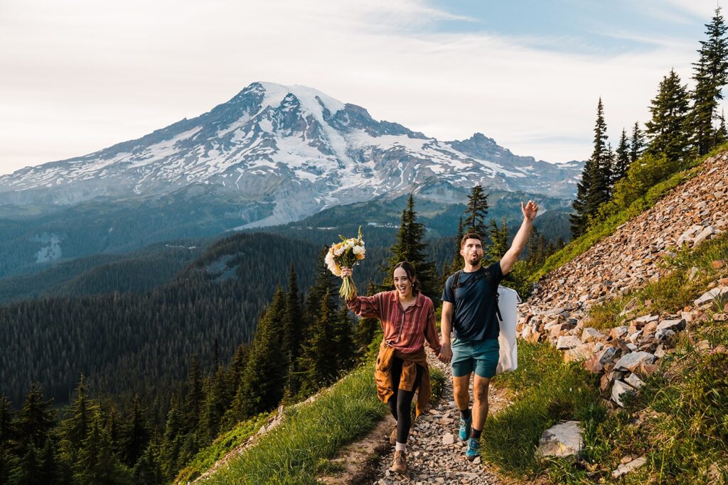 Bride and groom hold hands while hiking a mountain trail during their elopement in Mt Rainier National Park