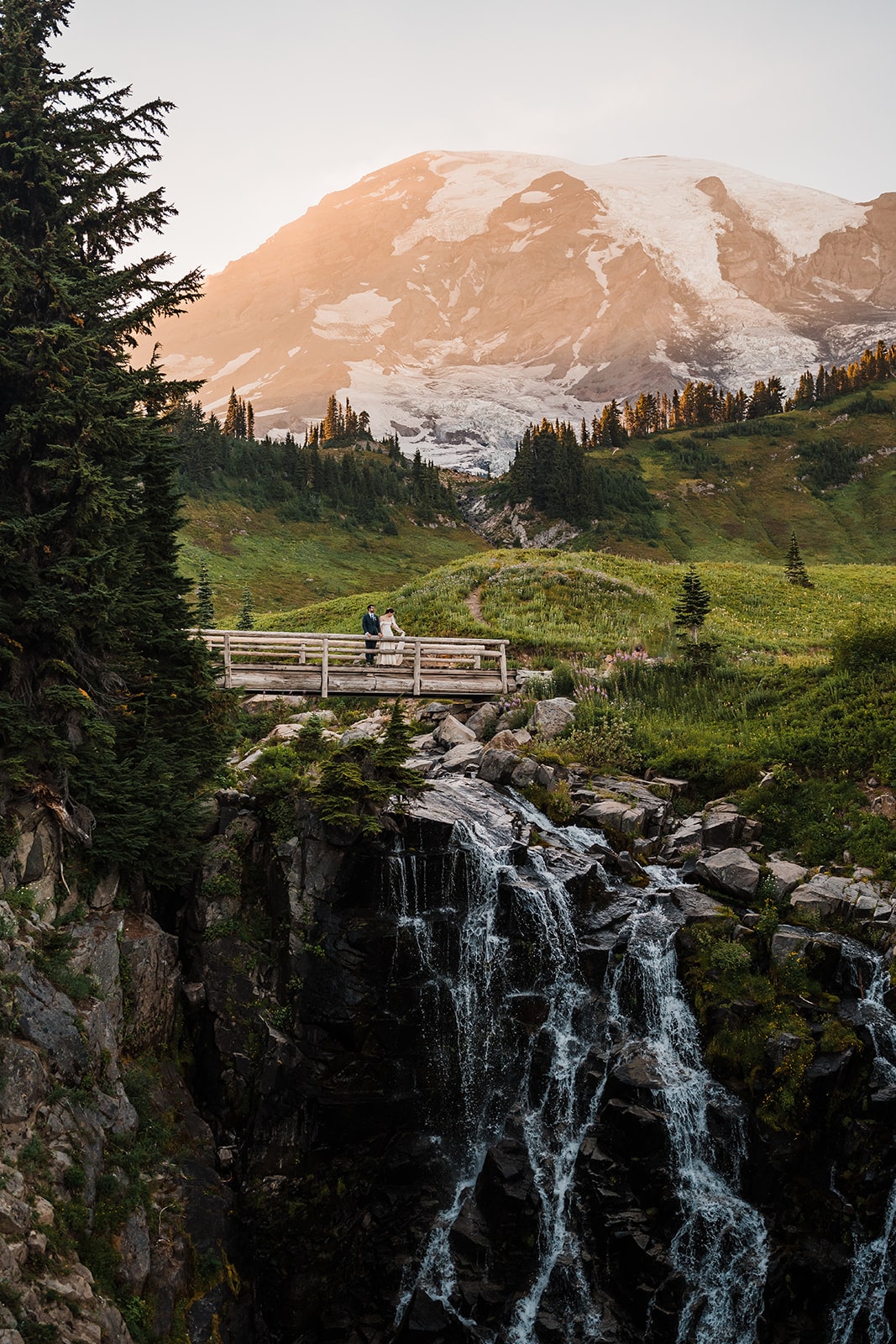 Bride and groom stand on a wood bridge over a waterfall during their elopement at Mt Rainier National Park