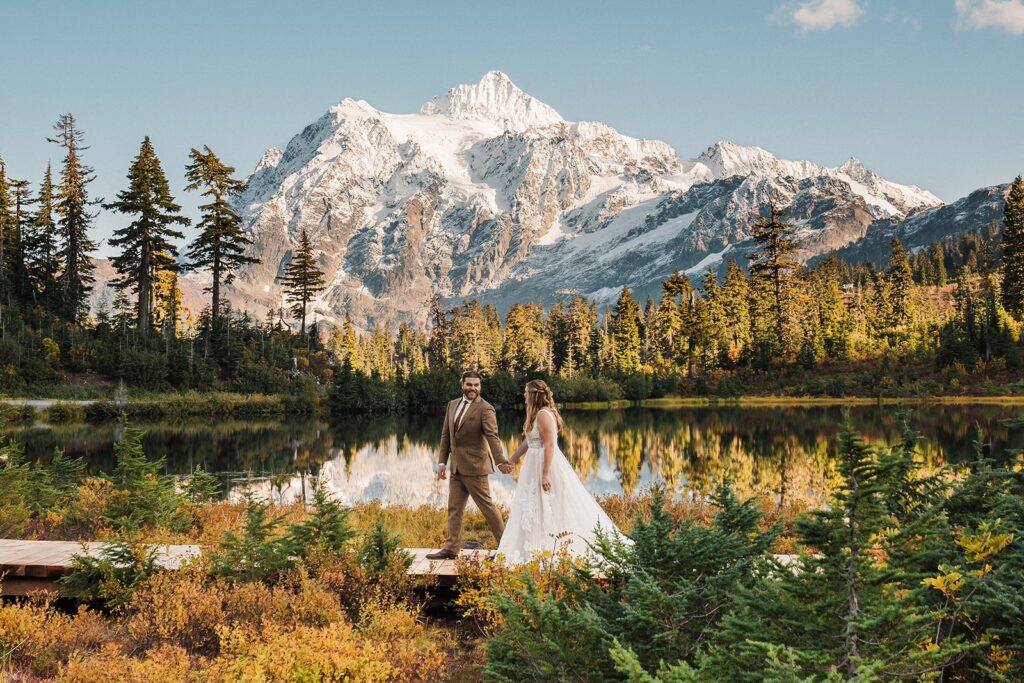 Bride and groom hold hands while walking around an alpine lake at their North Cascades National Park elopement